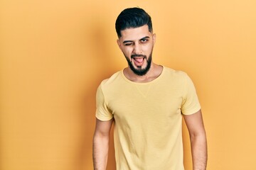 Handsome man with beard wearing casual yellow t shirt winking looking at the camera with sexy expression, cheerful and happy face.