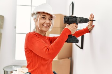 Middle age grey-haired woman smiling confident drilling wall at new home