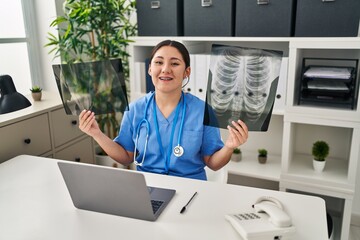 Young latin doctor woman holding x-ray smiling and laughing hard out loud because funny crazy joke.