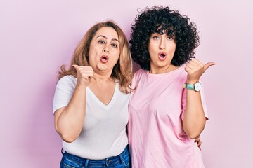 Middle east mother and daughter wearing casual clothes surprised pointing with hand finger to the side, open mouth amazed expression.