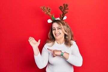 Middle age caucasian woman wearing cute christmas reindeer horns amazed and smiling to the camera...