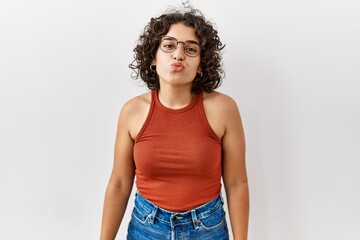 Young hispanic woman wearing glasses standing over isolated background looking at the camera blowing a kiss on air being lovely and sexy. love expression.