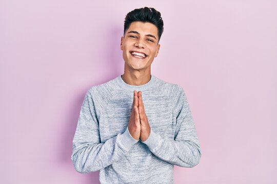 Young hispanic man wearing casual clothes praying with hands together asking for forgiveness smiling confident.