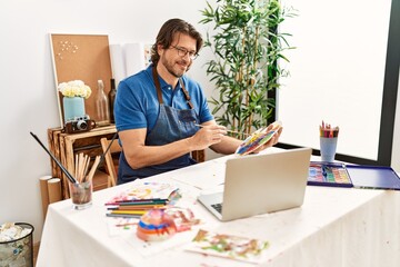 Middle age caucasian man smiling confident having online art class at art studio