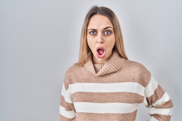 Young blonde woman wearing turtleneck sweater over isolated background in shock face, looking...