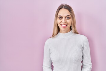 Obraz premium Young blonde woman wearing white sweater over pink background with a happy and cool smile on face. lucky person.
