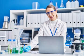 Young woman scientist smiling confident using laptop at laboratory