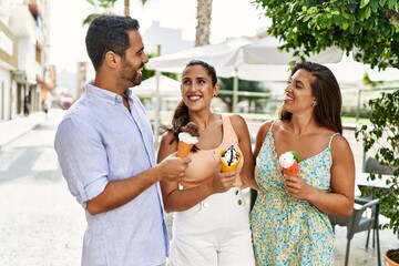 Three hispanic friends smiling happy eating ice cream at the city.