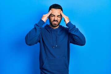 Handsome hispanic man with beard wearing casual sweatshirt with hand on head, headache because...