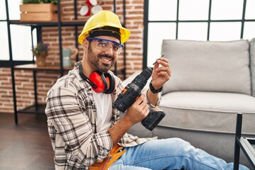 Young hispanic man worker smiling confident holding drill at home - obrazy, fototapety, plakaty