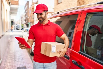 Young hispanic man courier using touchpad holding package at street
