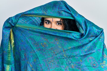 Young indian woman wearing sari covering head and face, doing elegant pose with traditional scarf