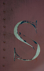 The letter S isolated on side of rusty metal shipping container with red burgundy or rust colored paint chipped weathered and grungy looking with peeling paint and rust spots vertical format 