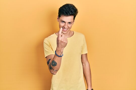 Young hispanic man wearing casual yellow t shirt beckoning come here gesture with hand inviting welcoming happy and smiling