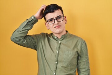 Non binary person standing over yellow background confuse and wonder about question. uncertain with doubt, thinking with hand on head. pensive concept.