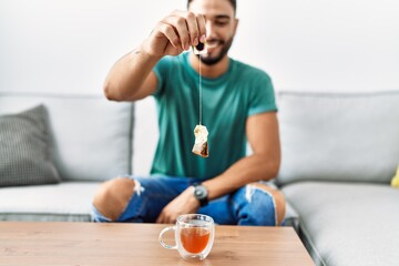Young arab man smiling confident holding tea bag at home
