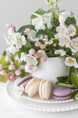Beautiful composition with delicious French macarons and spring flowers in a white cup. Sweet dessert, early spring white and pink flowers, wedding decor, bride morning