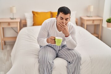 Young man drinking coffee yawning at bedroom