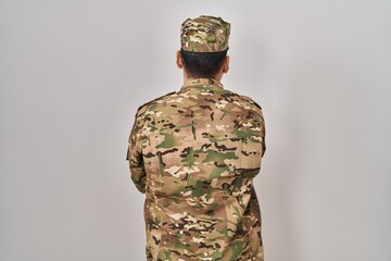 Young arab man wearing camouflage army uniform standing backwards looking away with crossed arms