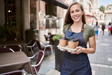 Young blonde woman wearing apron holding coffee at coffee shop