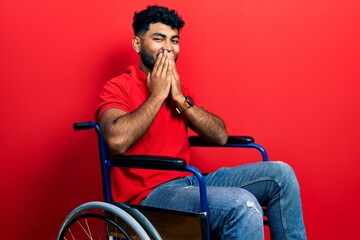 Arab man with beard sitting on wheelchair laughing and embarrassed giggle covering mouth with hands, gossip and scandal concept