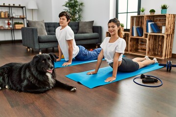 Young caucasian couple smiling happy training yoga with dog at home.
