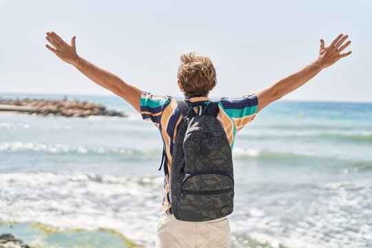 Young man tourist wearing backpack with arms open at seaside