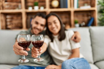 Young latin couple smiling happy toasting with red wine glass at home.