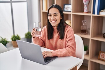 Obraz premium Young hispanic woman using laptop drinking water at home