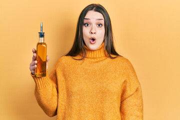 Young hispanic girl holding olive oil can scared and amazed with open mouth for surprise, disbelief...