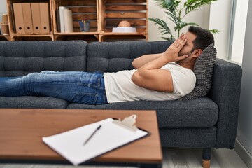 Young hispanic man stressed having mental therapy lying on sofa at psychology center
