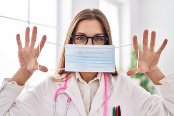 Young woman wearing doctor uniform covering mouth with medical mask at clinic