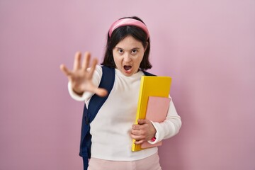 Woman with down syndrome wearing student backpack and holding books doing stop gesture with hands...