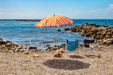 Sun umbrella and two chairs  on a  pebbly beach on sunny day at the blue sea background. Monterosso...