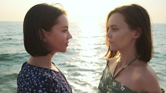 Two woman friends at sea beach. Girls looking at each other standing together.