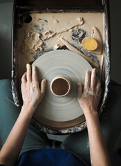Young female master working on a potter’s wheel, creates clay dishes. Ceramist young woman making...
