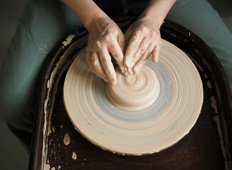 Young female master working on a potter’s wheel, creates clay dishes. Ceramist young woman making clay product on pottery lathe in studio, workshop, top view. Small business, hobby, ceramic concept.