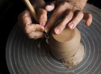 Ceramist at work using tools for creating handmade vase in studio, selective focus. Close up of female potter hands sharing handcraft crockery in studio. Small business, art, hobby concept.