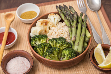 Baked broccoli, cauliflower and asparagus with brown rice, spices and lemon in clay bowl. Vegan...