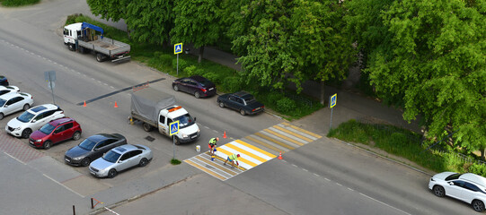 Road workers paint a crosswalk with yellow and white stripes, marking off the area with traffic...