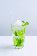 Fresh mojito made of fresh citrus fruit and green mint leaves. Glass with delicious beverage with crushed ice and straw on a light background. Cool Refreshing drink.