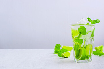 Fresh mojito with crushed ice in glass on white table. Cool refreshing drink made of fresh citrus fruit and slices of lime and mint on light background with copy space.
