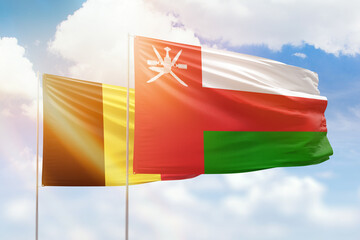 Sunny blue sky and flags of oman and belgium
