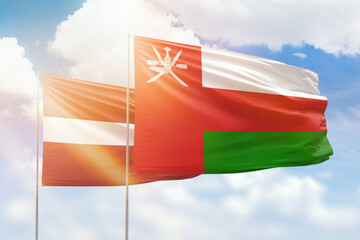 Sunny blue sky and flags of oman and latvia