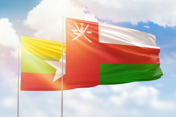 Sunny blue sky and flags of oman and myanmar