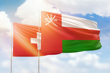 Sunny blue sky and flags of oman and switzerland