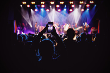 Fototapeta na wymiar Holding a smartphone to record music concert. Mobile phone at a summer festival.