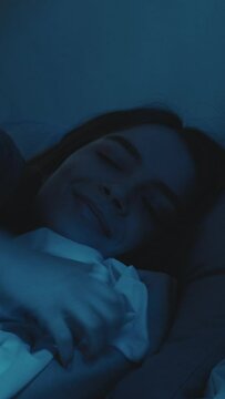 Good night. Pleased woman. Sweet dreams. Pretty lady lying down in comfortable bed turning off light falling asleep in dark room interior. Vertical video.