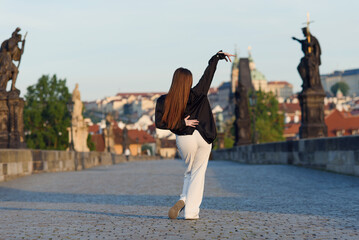 Young woman in casual stylish clothes dancing on the stone bridge of old town in a Prague. Active...