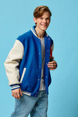 a happy guy in a white t-shirt and a trendy teen bomber jacket stands smiling looking at the camera on a plain background with space for text. studio photo